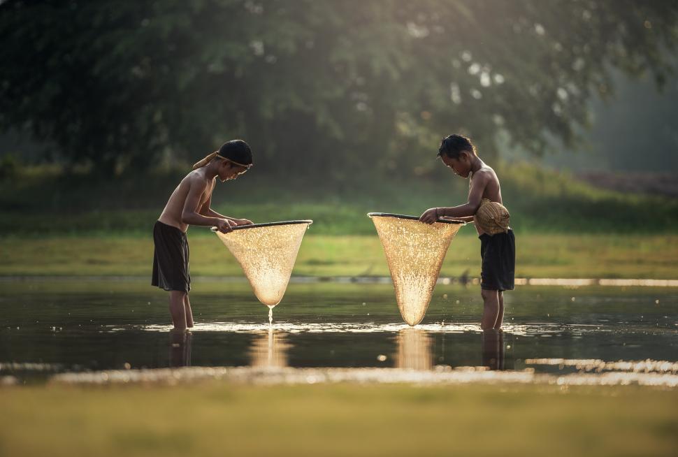 Free Image of Two Boys Stand in Water With Fishing Nets 
