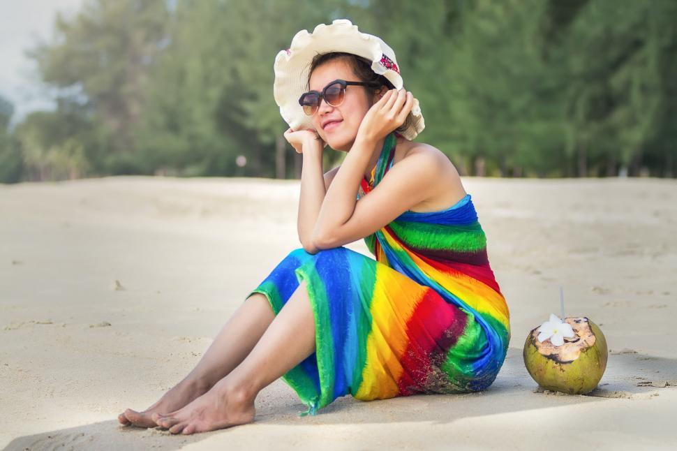 Free Image of Woman Sitting on Beach Next to Coconut 