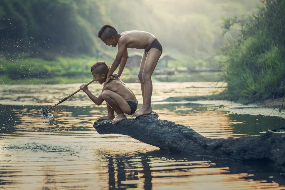 Free Image of Two Boys Sitting on a Log in the Water 