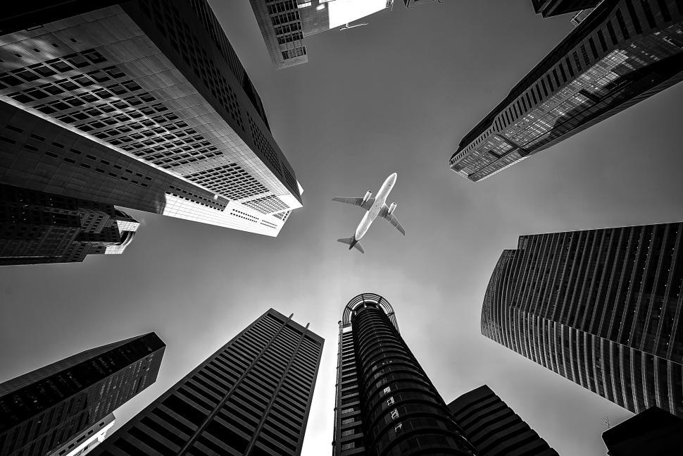 Free Image of Plane Flying Through Sky Between Tall Buildings 