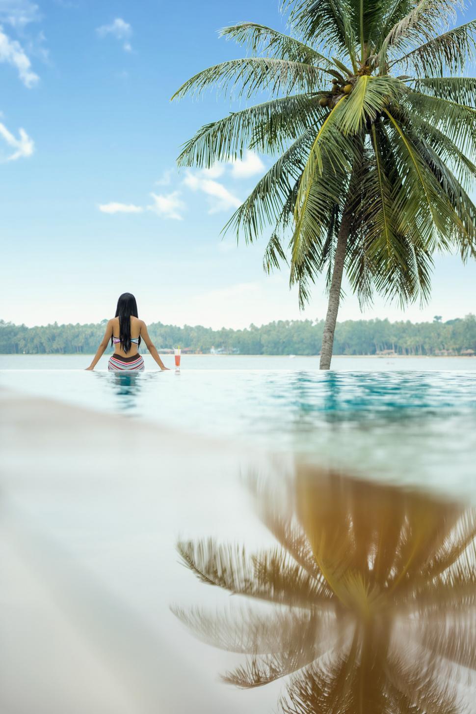 Free Image of Woman Sitting in Pool Next to Palm Tree 