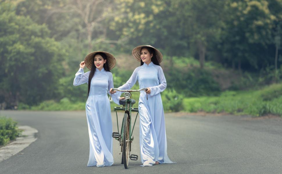 Free Image of Two Women in Blue Dresses Standing Next to a Bike 