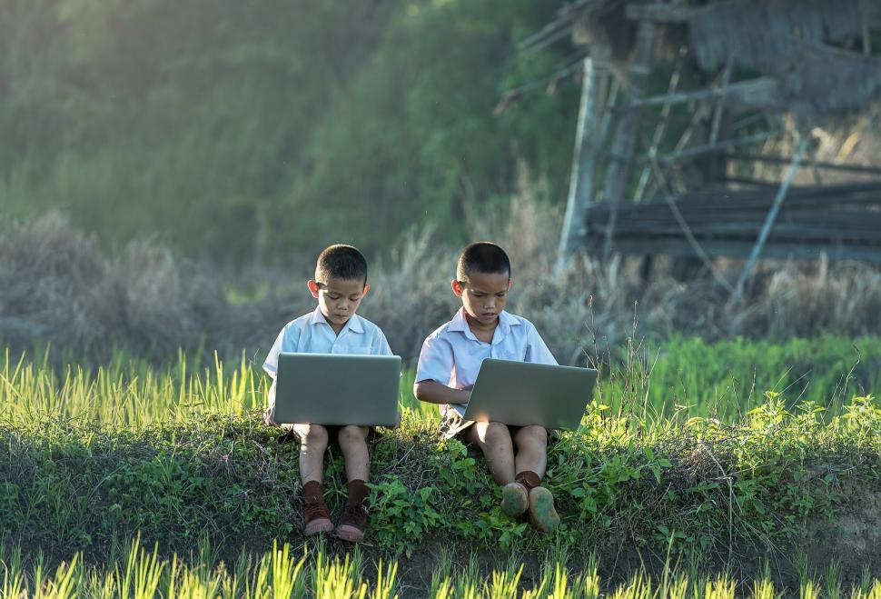 Free Image of Two Young Boys Sitting on a Patch of Grass Using Laptops 