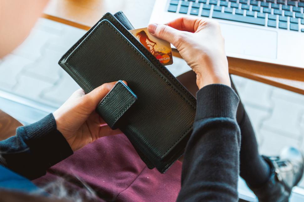 Free Image of Person Holding Wallet in Front of Laptop 
