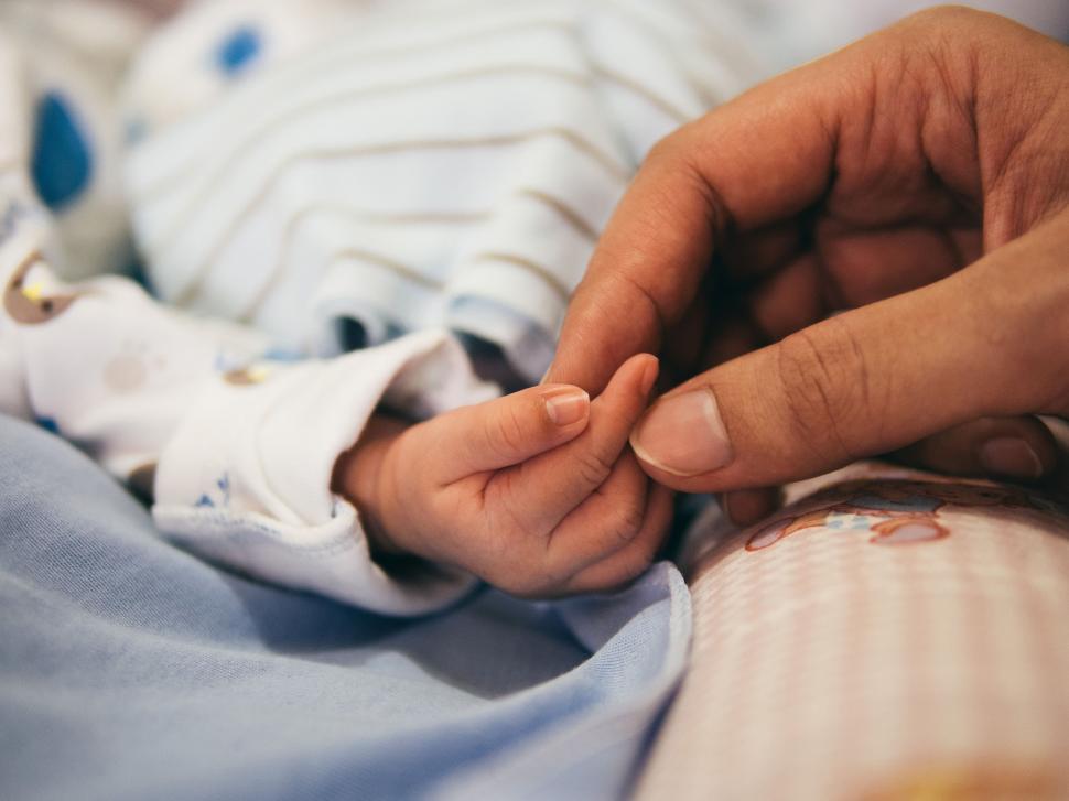 Free Image of Person Holding Babys Hand on Bed 