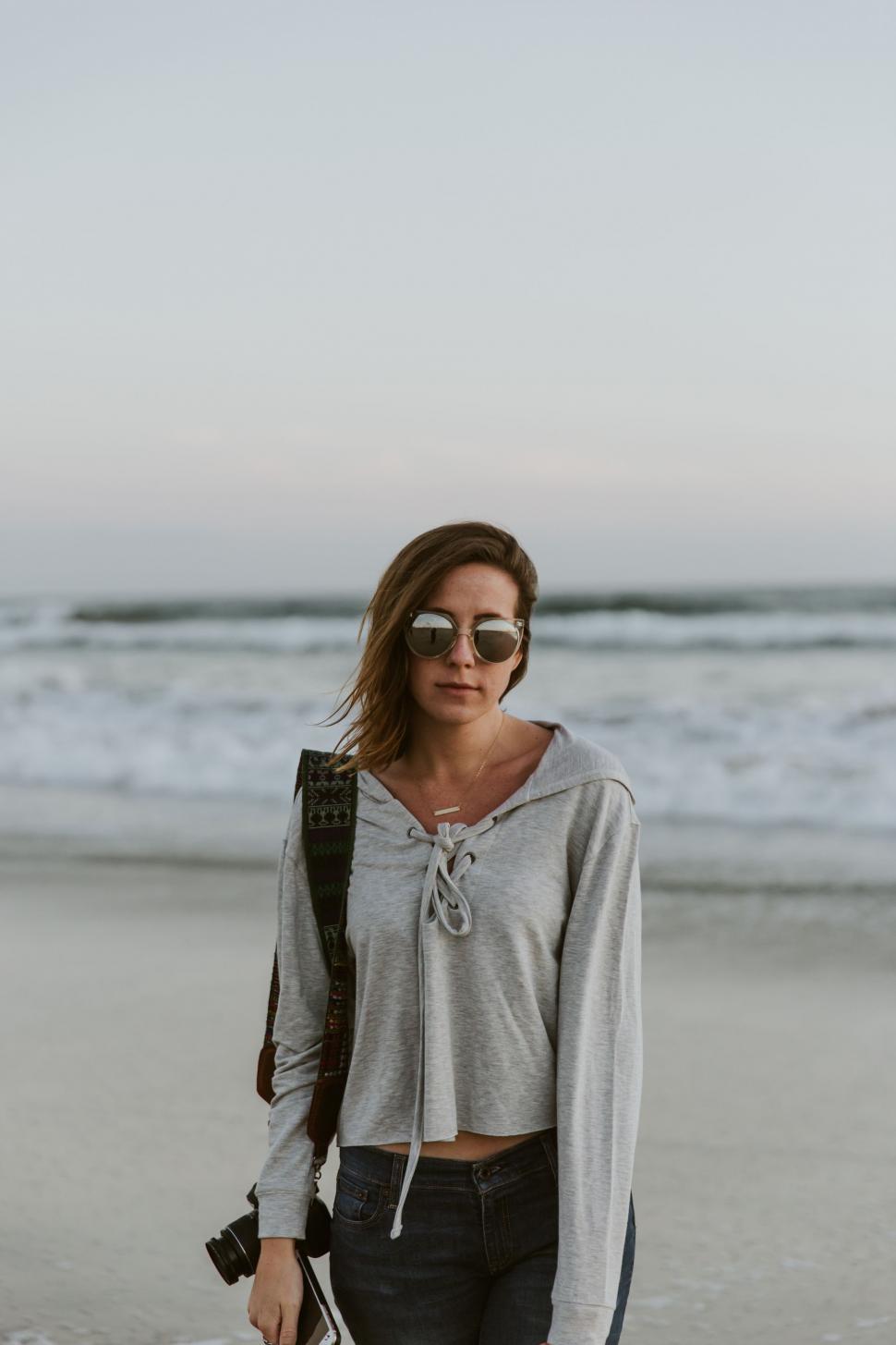 Free Image of Woman Standing on Beach With Camera 