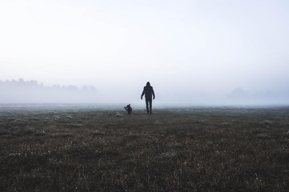 Free Image of Person Walking With Dog in Foggy Field 