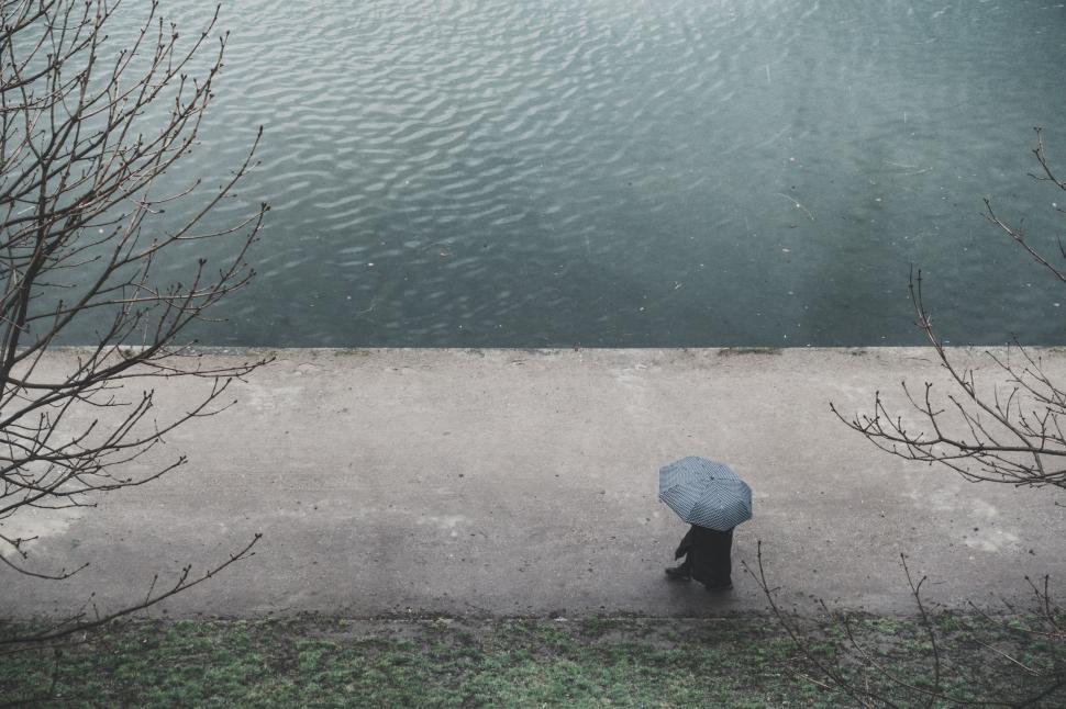 Free Image of Person Walking With Blue Umbrella Along Water 