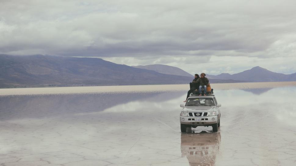 Free Image of Two People Standing on Top of a Car in the Middle of a Body of Water 