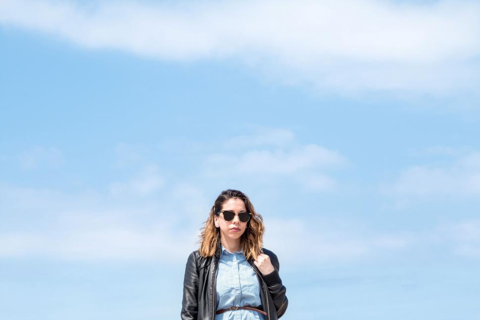 Free Image of Woman in Black Jacket and Sunglasses Standing on Beach 