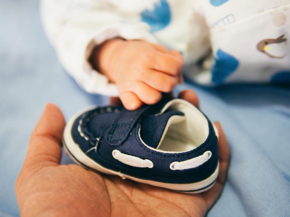 Free Image of Hand Holding Babys Shoe on Bed 