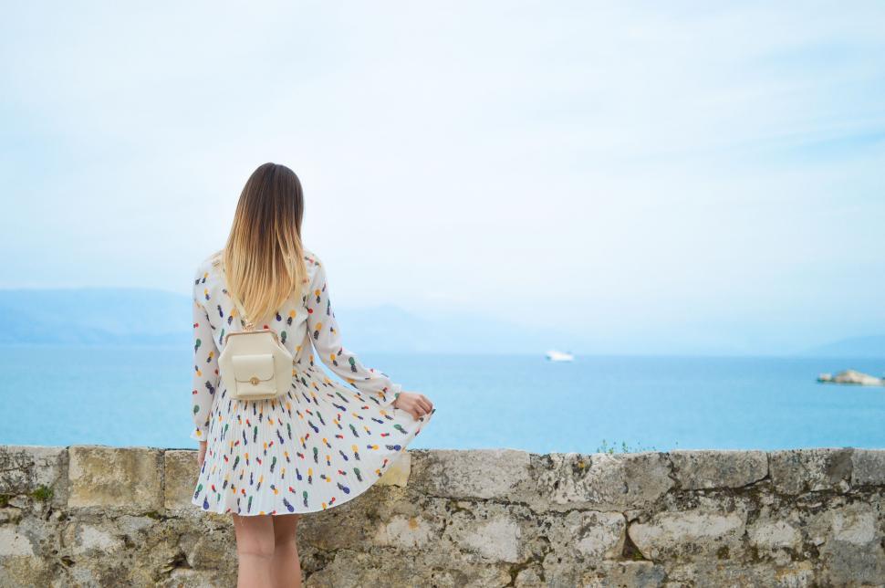 Free Image of Woman Standing on Stone Wall Looking at Ocean 