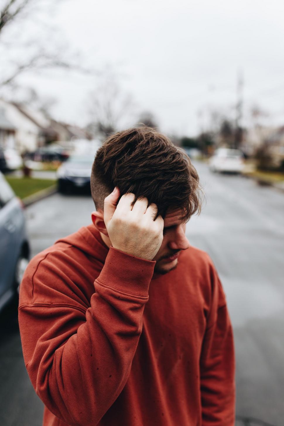 Free Image of Man in Red Sweatshirt Holding Head in Hands 