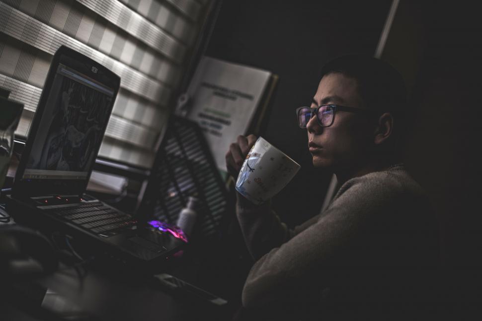 Free Image of Man Holding Coffee Cup Working on Laptop 