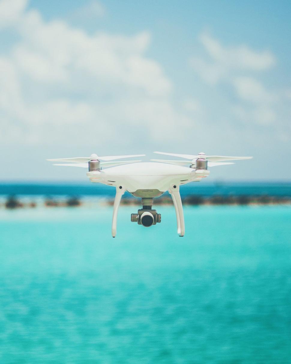 Free Image of Small White Camera Flying Over Body of Water 