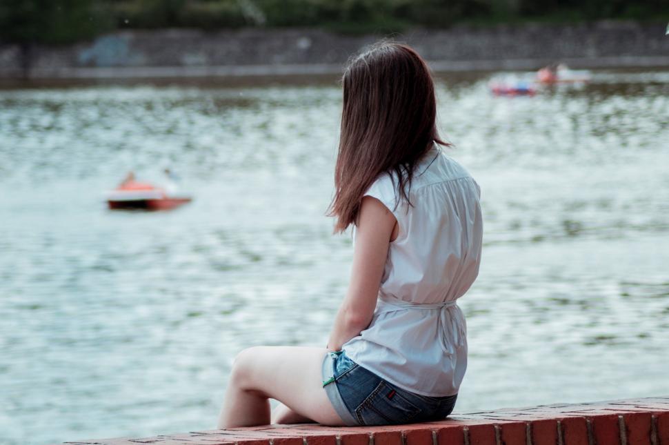 Free Image of Woman Sitting on Brick Wall by Water 