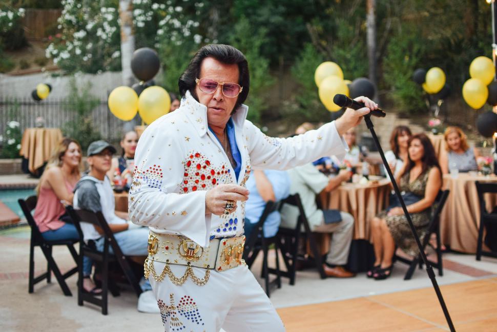 Free Image of A Man in an Elvis Outfit Holding a Microphone in Front of a Group 