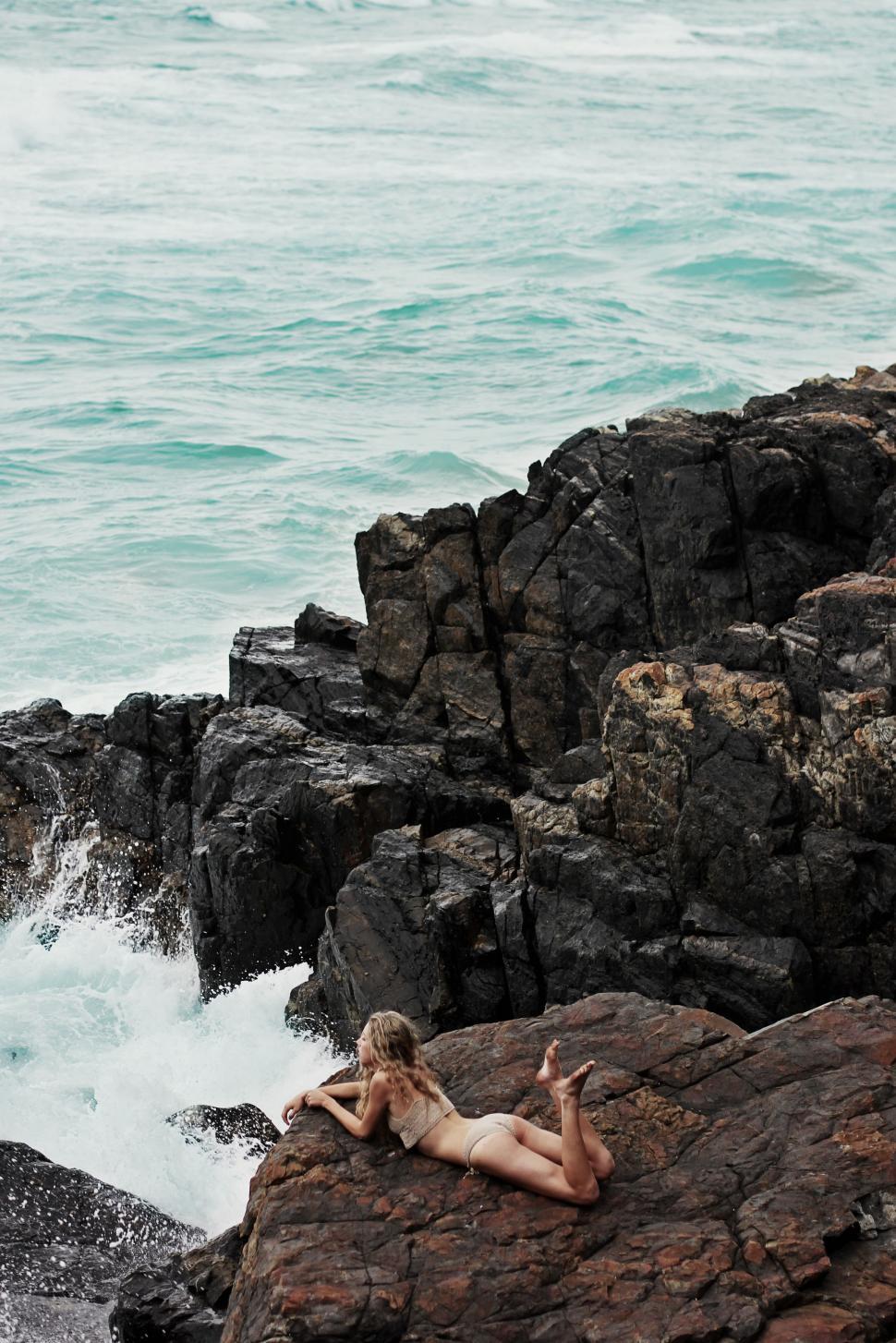 Free Image of Woman Laying on Rock by the Ocean 
