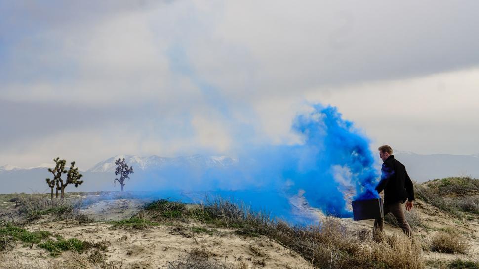Free Image of Man Standing on Top of Hill Next to Blue Cloud of Smoke 