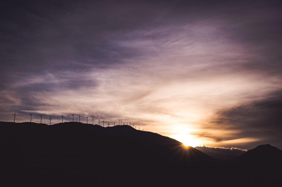 Free Image of Sun Setting Behind Hill With Row of Windmills 