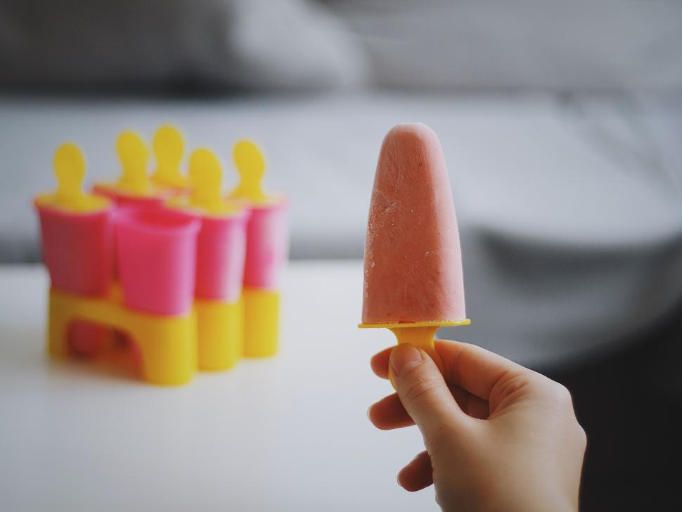 Free Image of Hand Holding Popsicle Next to Row of Plastic Cups 