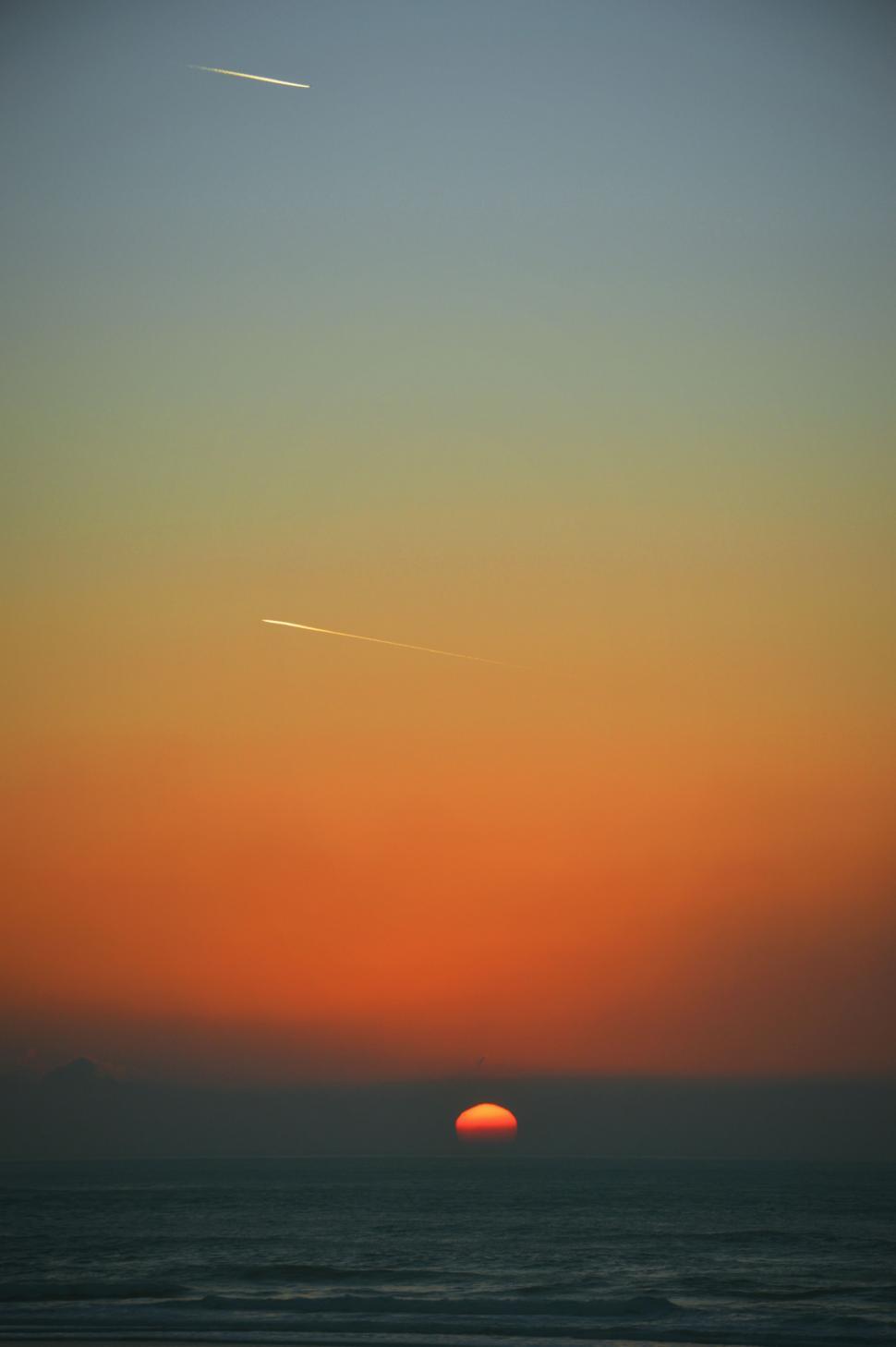 Free Image of Sun Setting Over Ocean With Plane in Sky 