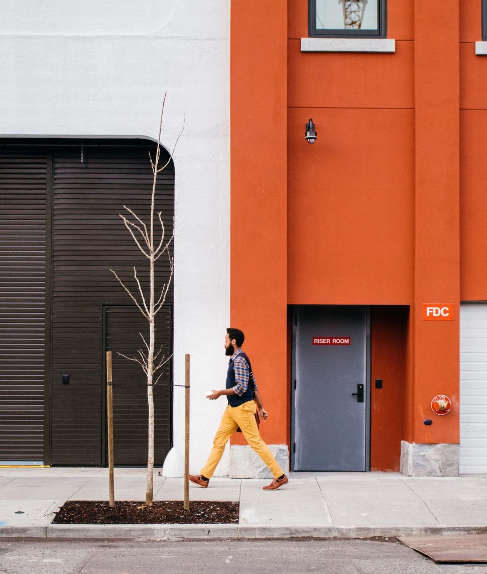 Free Image of Man Walking Past a Tall Orange Building 