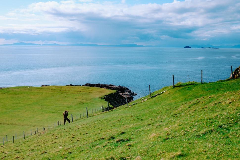 Free Image of Person Walking Up Grassy Hill Next to Body of Water 