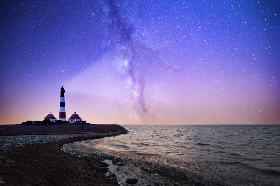Free Image of Lighthouse Illuminating Rocky Shore Under Night Sky 