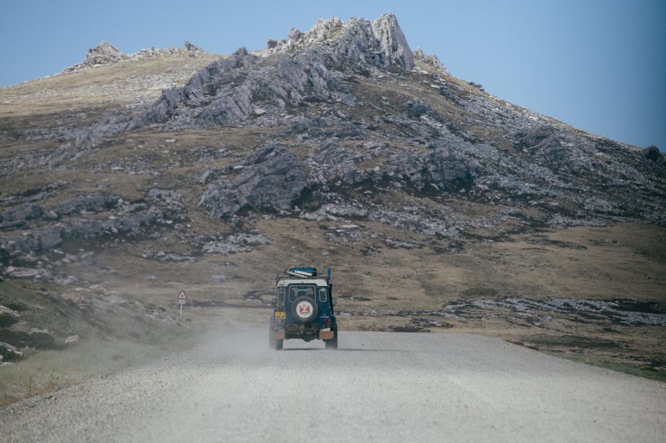 Free Image of Jeep Driving Down Dirt Road in Front of Mountain 