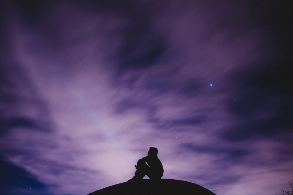 Free Image of Man Sitting on Top of Hill Under Purple Sky 