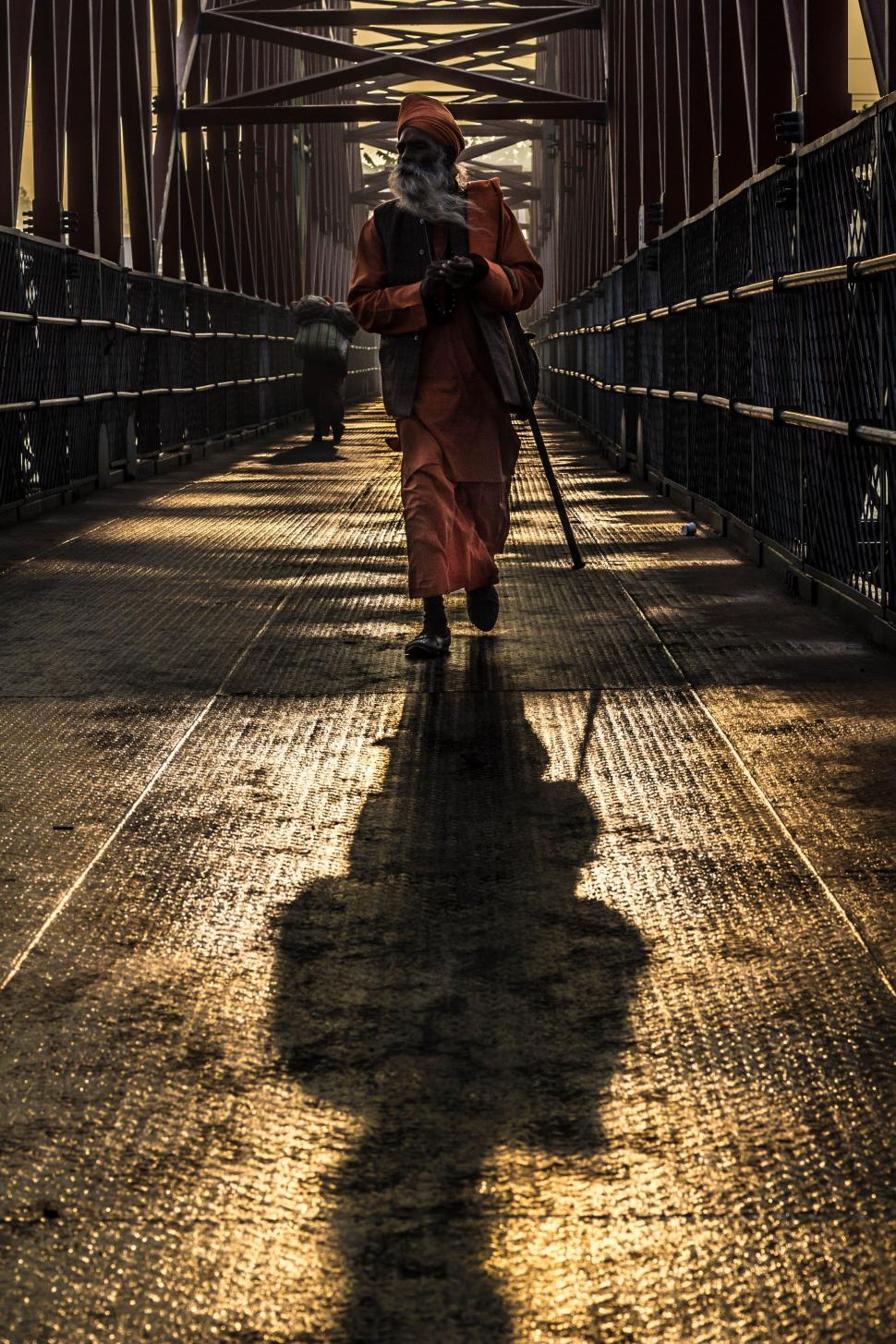 Free Image of Man Walking Across Bridge With Long Stick 