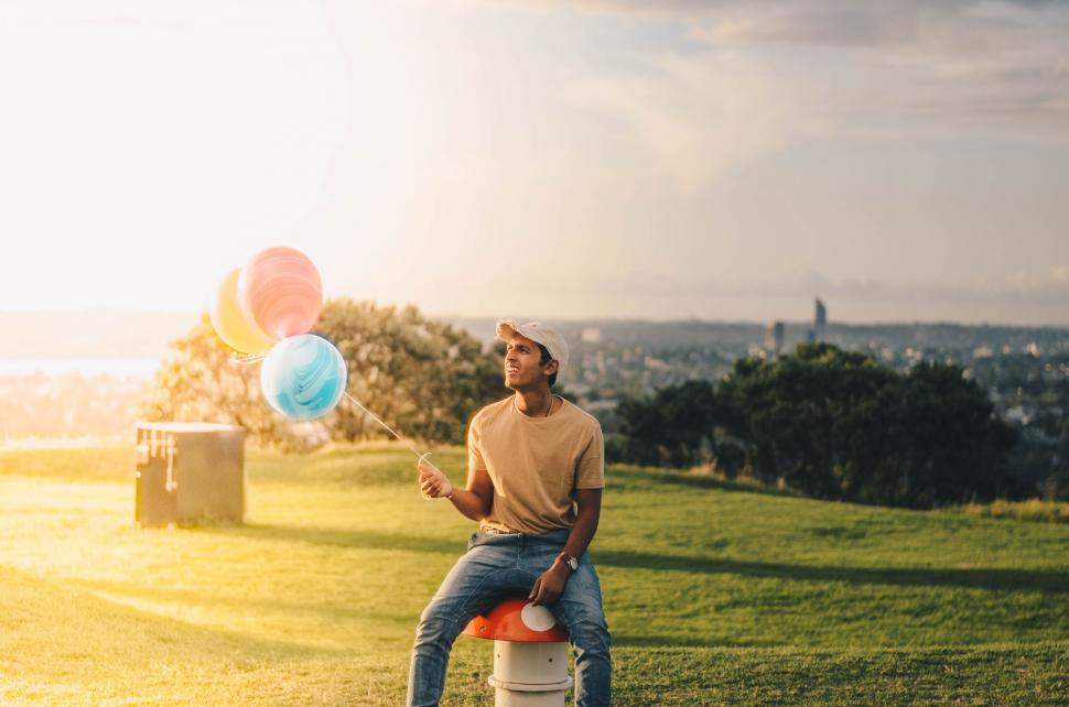 Free Image of Man Sitting on Fire Hydrant Holding Balloons 