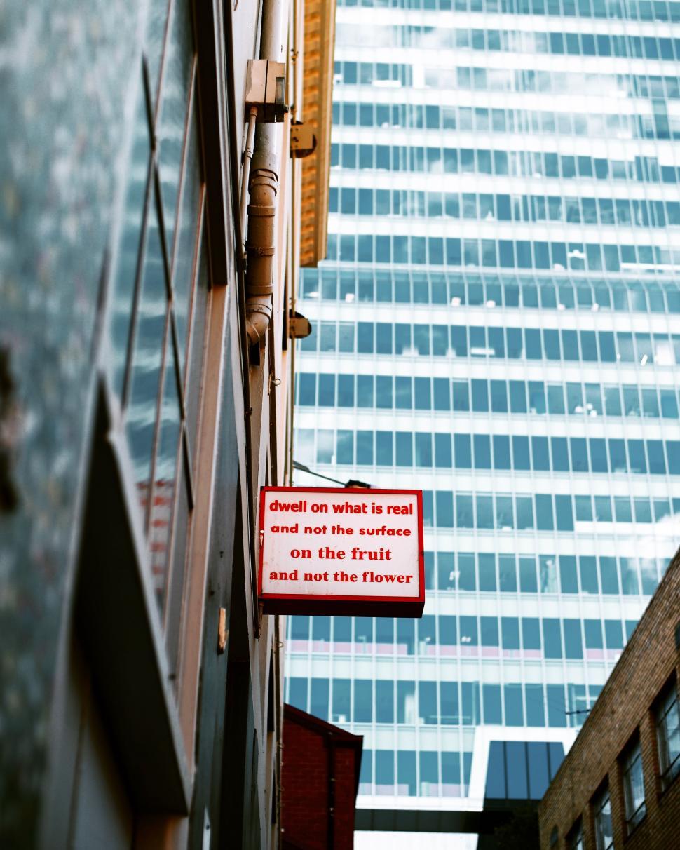 Free Image of Red Sign Hanging From Side of Tall Building 
