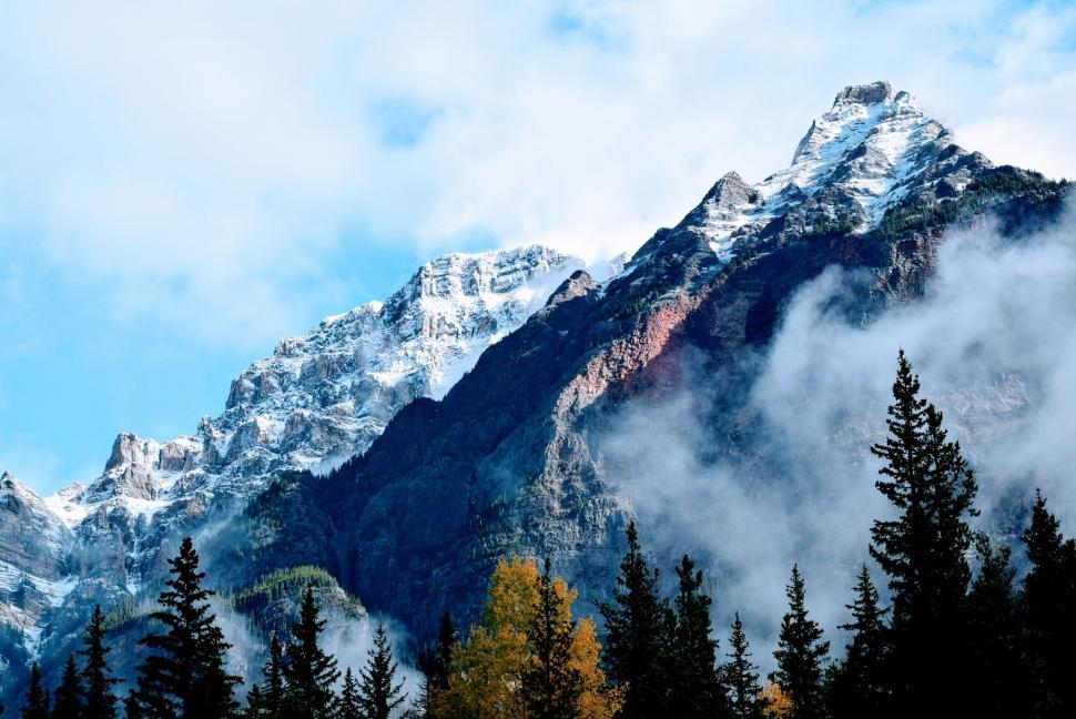 Free Image of Mountain Covered in Clouds and Trees Under Blue Sky 