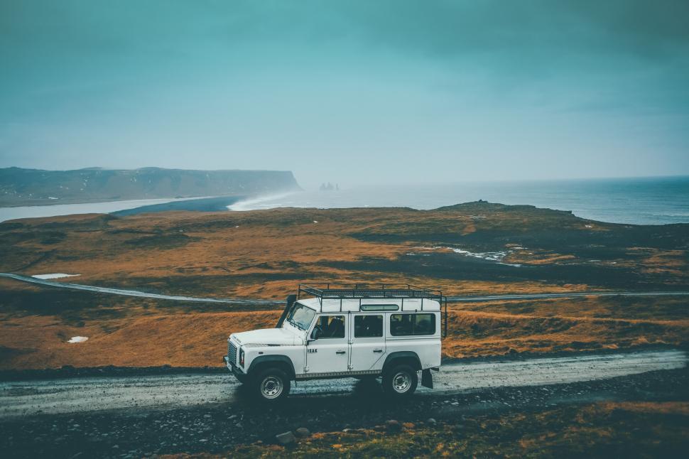 Free Image of White Jeep Driving Down Road Next to Body of Water 