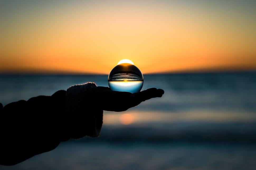Free Image of Hand Holding Glass Ball With Sunset Background 