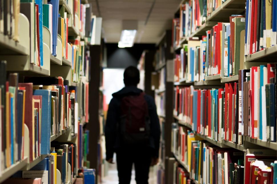 Free Image of Person Walking Down Long Aisle of Books 