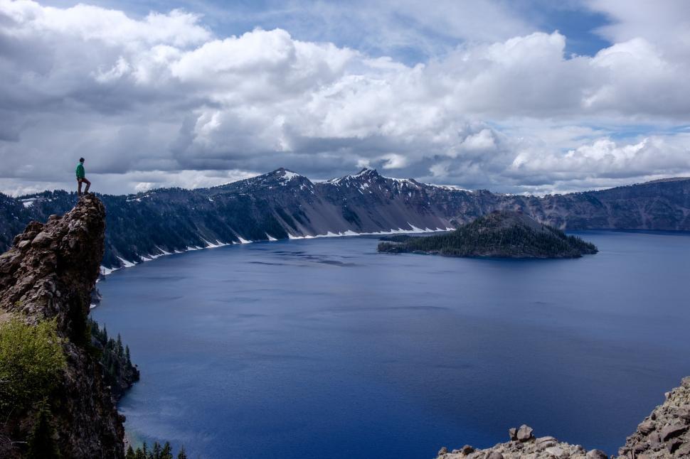 Free Image of Man Standing on Top of a Mountain by a Lake 