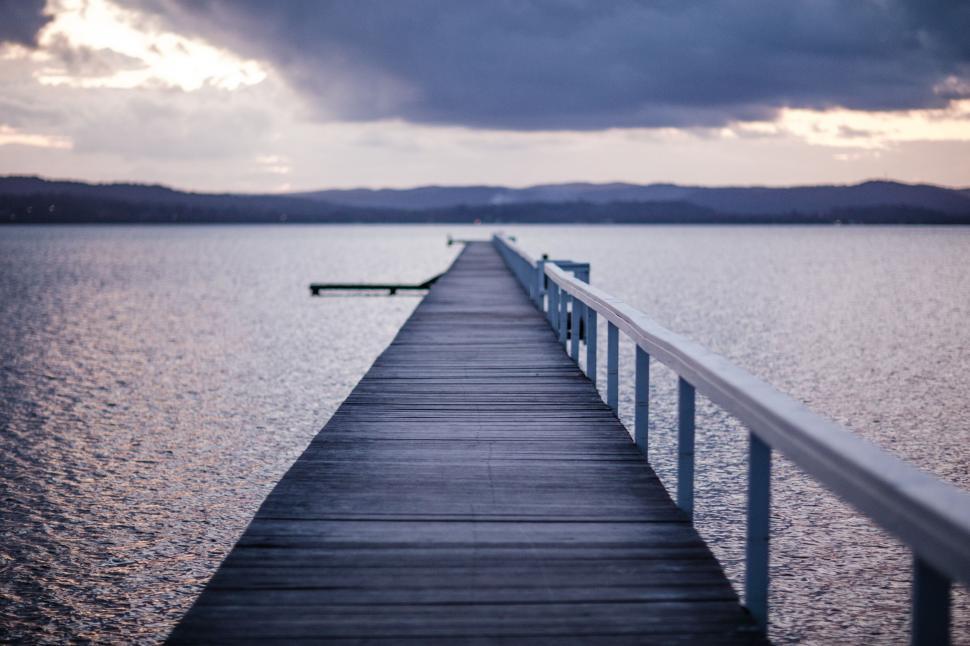 Free Image of Long Pier Extending Into Ocean Under Cloudy Sky 