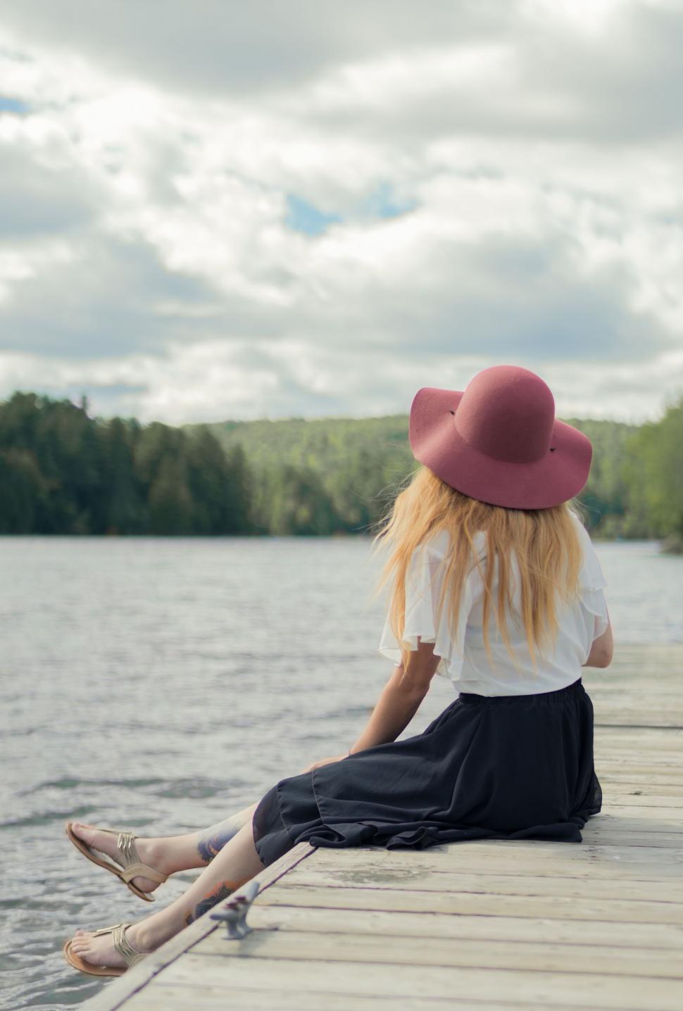 Free Image of Woman Sitting on Dock With Hat 