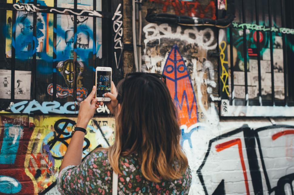 Free Image of Woman Taking a Picture of Graffiti on a Wall 