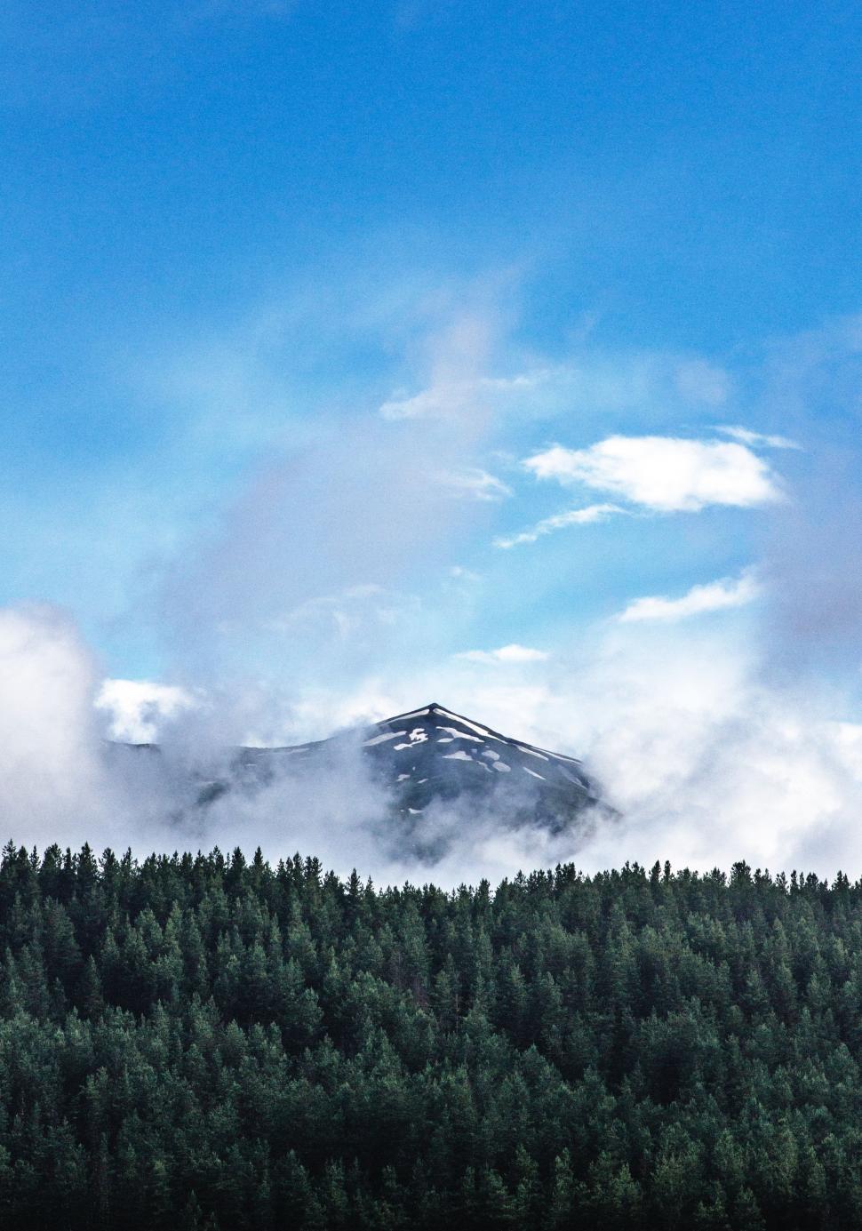 Free Image of Mountain Covered in Clouds and Trees Under a Blue Sky 