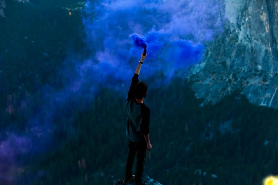 Free Image of Man Standing on Mountain Holding Blue Object 