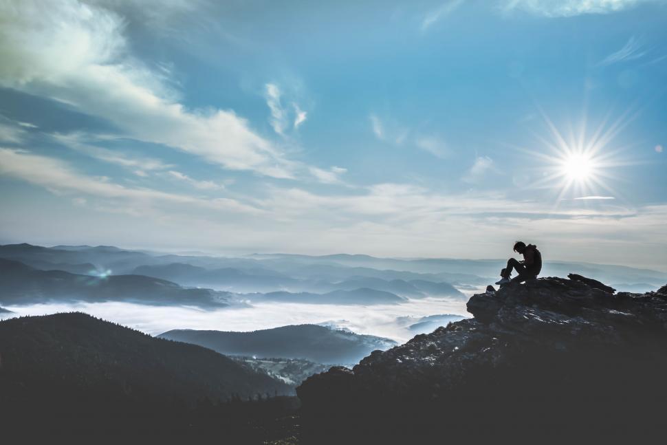 Free Image of Person Sitting on Mountain Top With Sky Background 