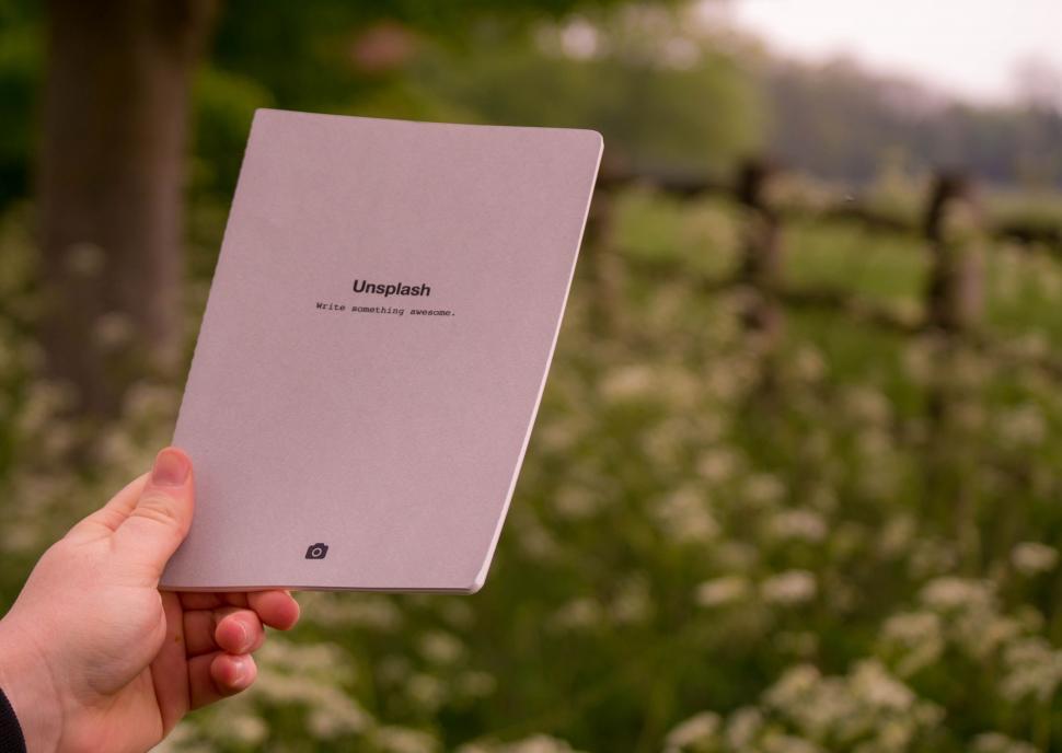 Free Image of Hand Holding White Tablet in Front of Field of Flowers 