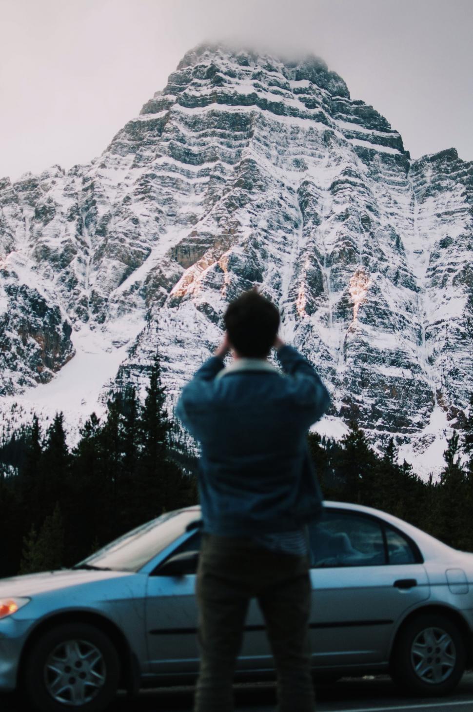 Free Image of Man Standing Next to Parked Car in Front of Snow Covered Mountain 
