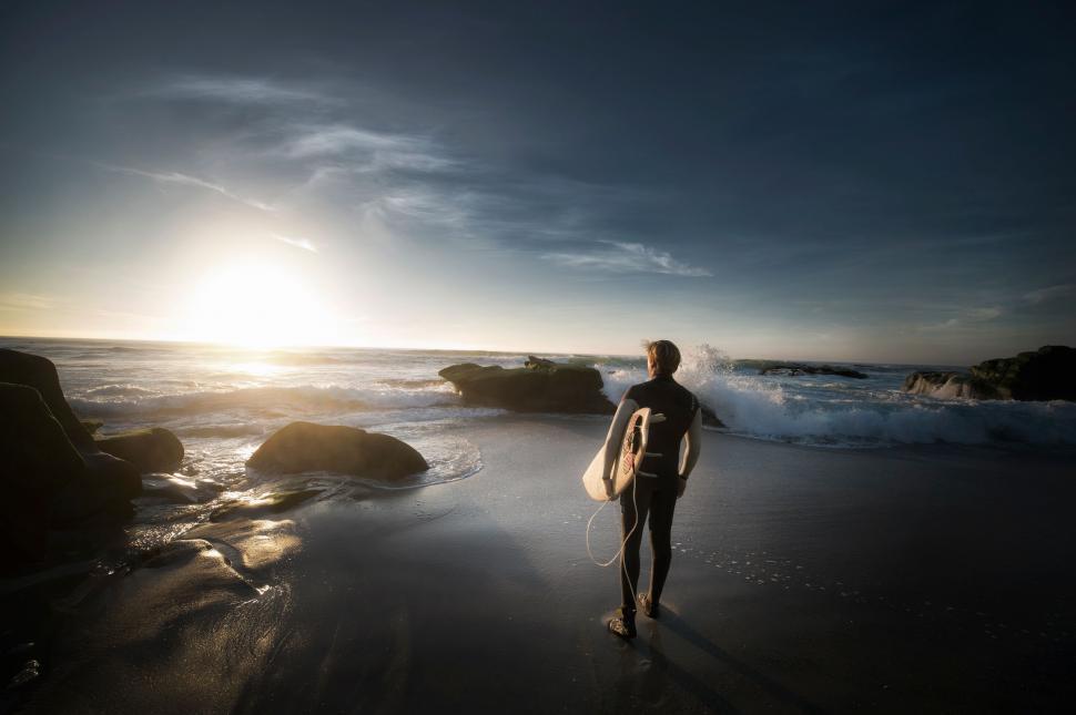 Free Image of Man Standing on Top of Beach Holding Surfboard 