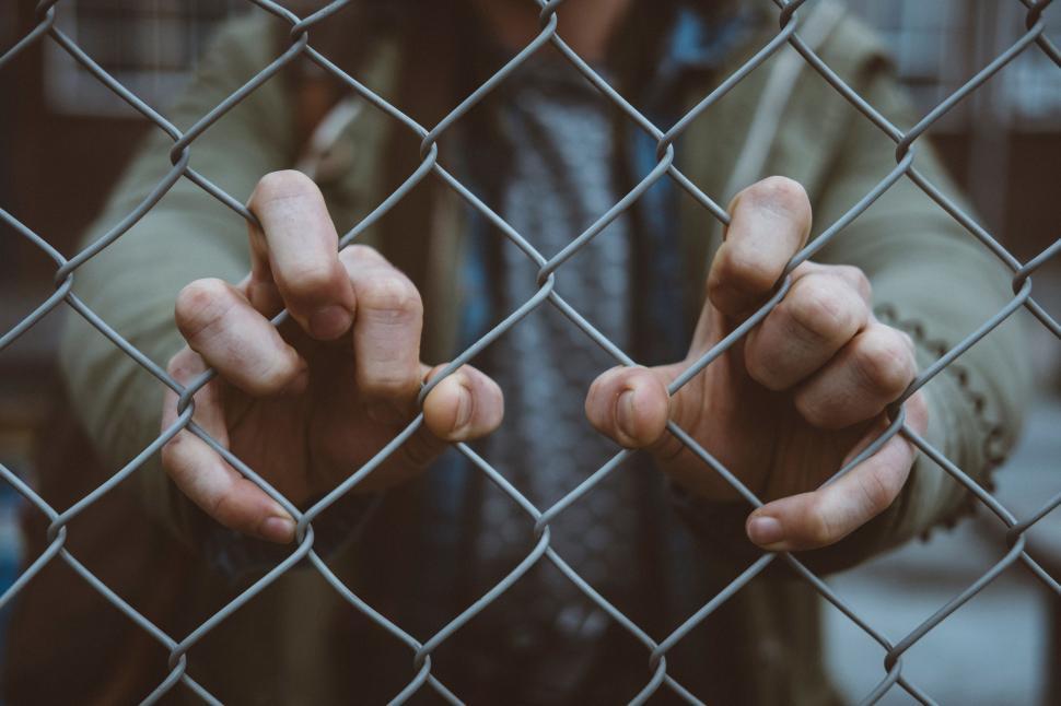 Free Image of Man Behind Chain Link Fence Holding Hands 