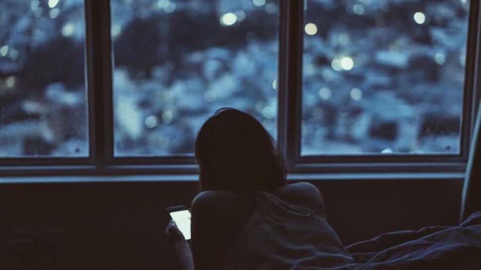 Free Image of Person Sitting on Bed Looking Out Window 